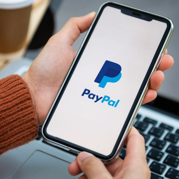 Man holding smartphone with open PayPal app on laptop background