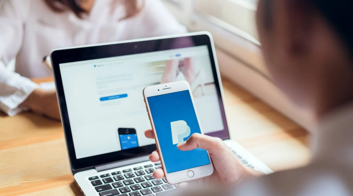 Girl holding a smartphone with the PayPal application on the background of a laptop