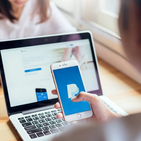 Girl holding a smartphone with the PayPal application on the background of a laptop