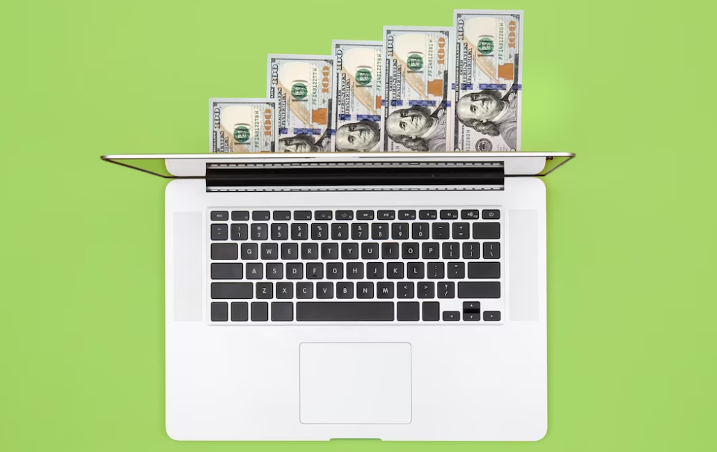 Laptop and dollar bills on color background flat lay