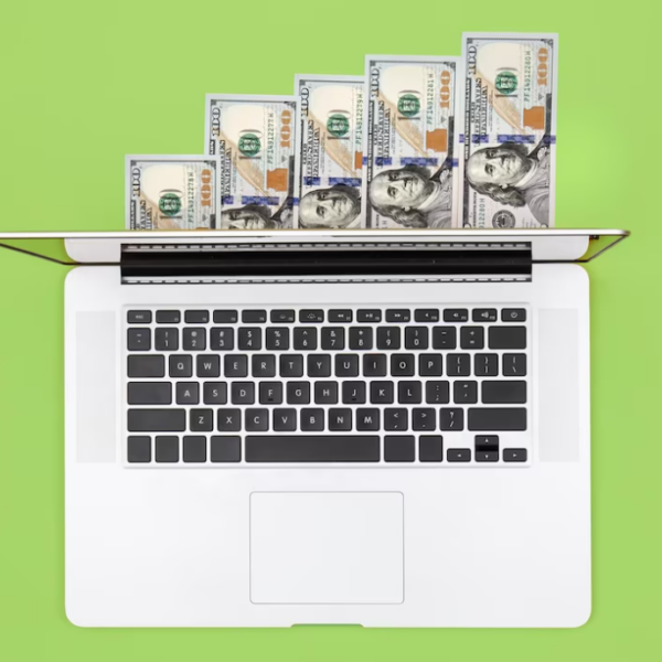Laptop and dollar bills on color background flat lay