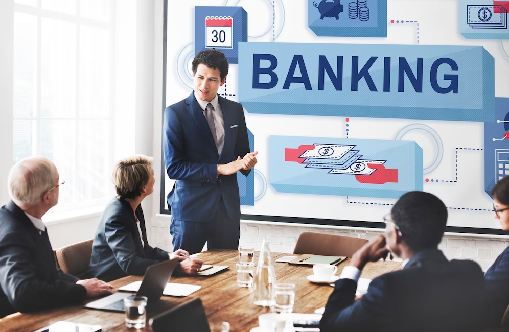 A group of people in a meeting, with one person standing and discussing and the term 'banking' is on the screen