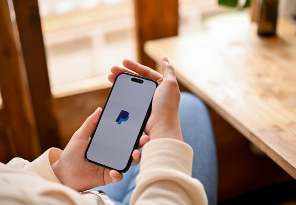 Person holding a phone with the PayPal logo displayed on the screen