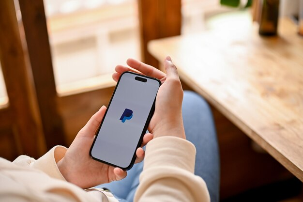 Person holding a phone with the PayPal logo displayed on the screen