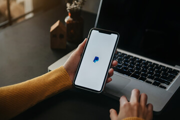 Person using a phone in front of a laptop with a PayPal logo on the screen