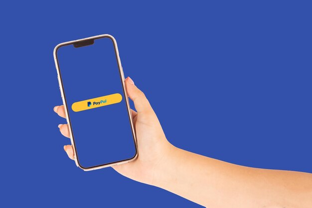 Hand holding a phone displaying the PayPal logo on a blue background
