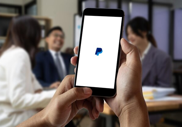 Man holding a smartphone with an open PayPal application against the background of colleagues